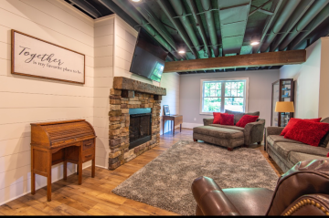 A living room with wood floors, a stone and wooden fire place, and modern exposed pipe ceiling showing the work of ATM Contracting LLC.