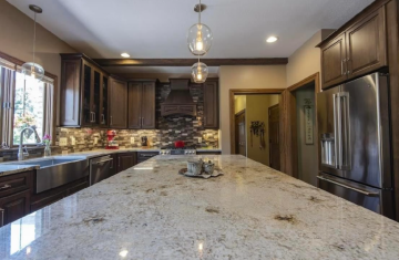 A kitchen with a large island, a back splash that is multicolored and brown and glass cabinets showing the building skills of ATM Contracting LLC.