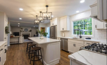 A kitchen with an island with cabinets on one side and three barstools on the other.  The backsplash is title and goes to the ceiling showing the installation skills of ATM Contracting LLC.