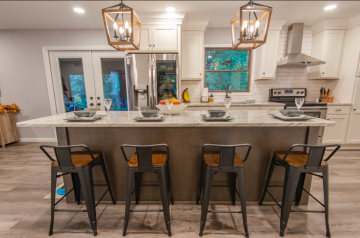 An island with four bar stool chairs stuck under the island and in the background the rest of the kitchen.