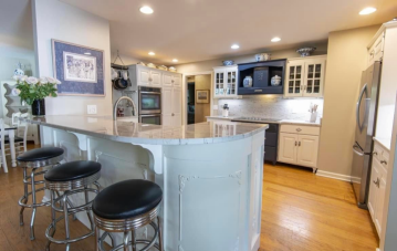 A higher counter rounded counter top with three bar stools under it. It has intricate wood work and overlooks the kitchen that has mixed styled cabinets showing the wood working skills of ATM Contracting LLC.