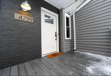 The front wooden porch of a brick black house with grey siding that was made modern by ATM Contracting LLC. 