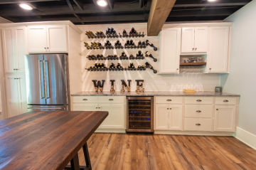 A kitchen with open wine racks, a bar area, and a wine refrigerator in between cabinets. 