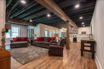 A Livingroom with wooden floors exposed pipes and wooden beams, and columns with a bar in the background showing the construction skills of ATM Contracting LLC.