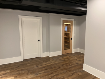 Another view of the wooden hallway with wooden floors showing two doors. One door has a glass panel and leads to the wall to wall wine rack.