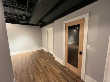 A hallway with two doors, wooden floors and an industrial styled ceiling.